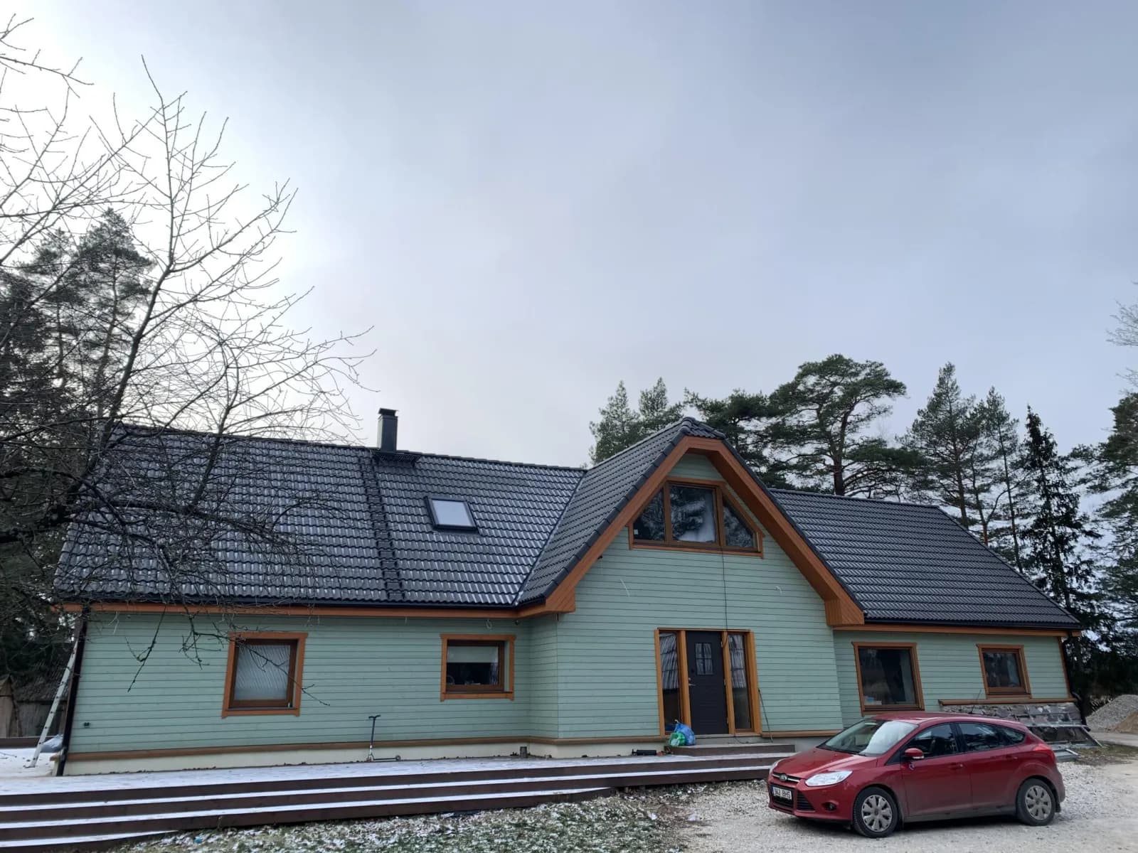 Valmis eramu tumeda viilkatusega, punane auto sõiduteel